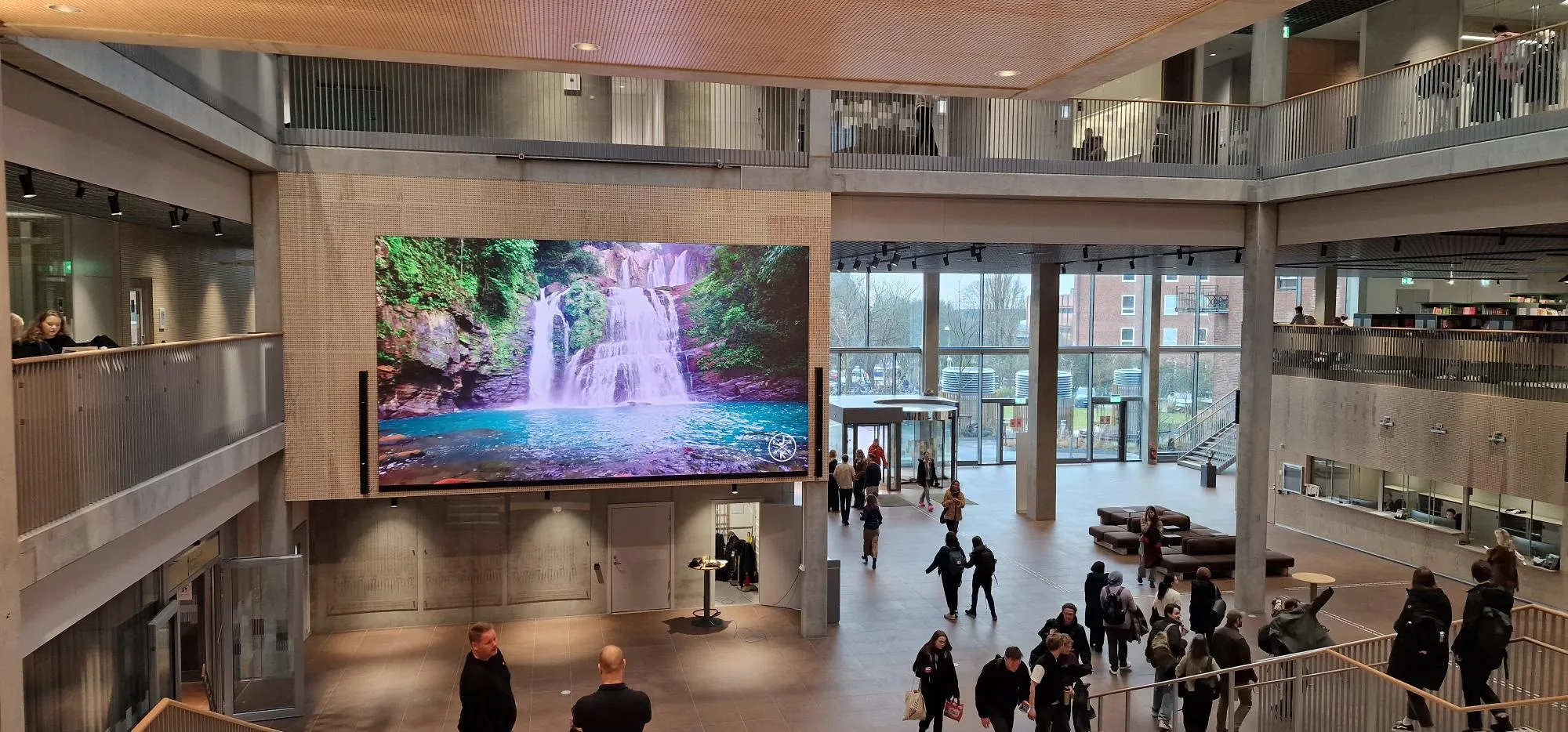 Ljust atrium i flera plan med stor LED-skärm som visar ett vattenfall